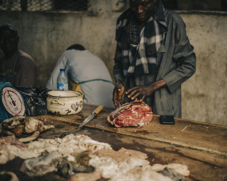 A skilled butcher preparing fresh meat at an indoor market stall with various cuts displayed.